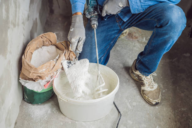 istock Young male painter kneads putty with water in a bucket using a hand-held mixer for building mixes 1086182990