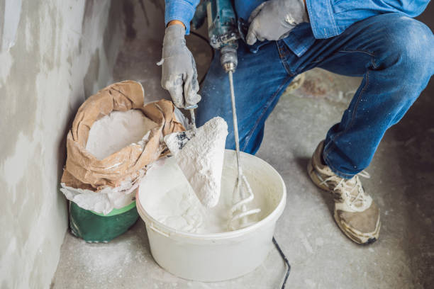 Young male painter kneads putty with water in a bucket using a hand-held mixer for building mixes