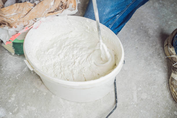 Young male painter kneads putty with water in a bucket using a hand-held mixer for building mixes