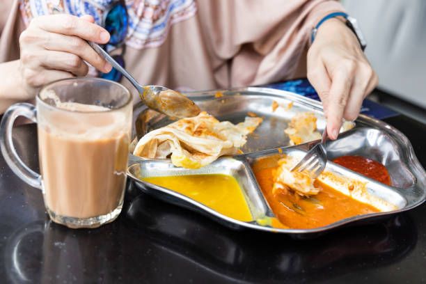 Person eating roti prata or canai with curry and dhal Roti prata or canai set with curry, dhal and sambal. Favorite breakfast in Malaysia roti canai stock pictures, royalty-free photos & images