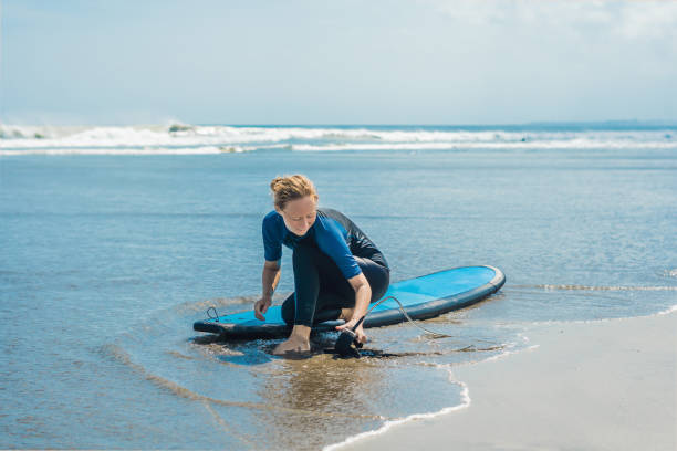 istock Summer time and active rest concept. Young surfer woman beginner fastens leash across leg, going to surf on big barral waves on ocean, dresseed in boardies, poses aganist sky on hot sunny day 1086193864