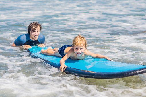 Father teaching his young son how to surf in the sea on vacation or holiday. Travel and sports with children concept.