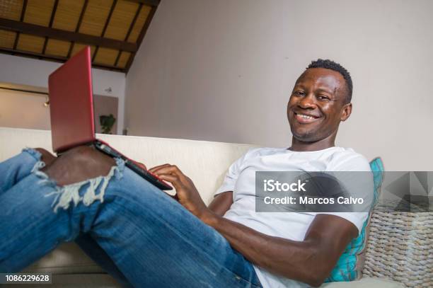 Young Attractive And Happy Successful Black Afro American Man Networking With Laptop Computer At Living Room Couch Smiling Cheerful And Satisfied In Internet Business Success Concept Stock Photo - Download Image Now