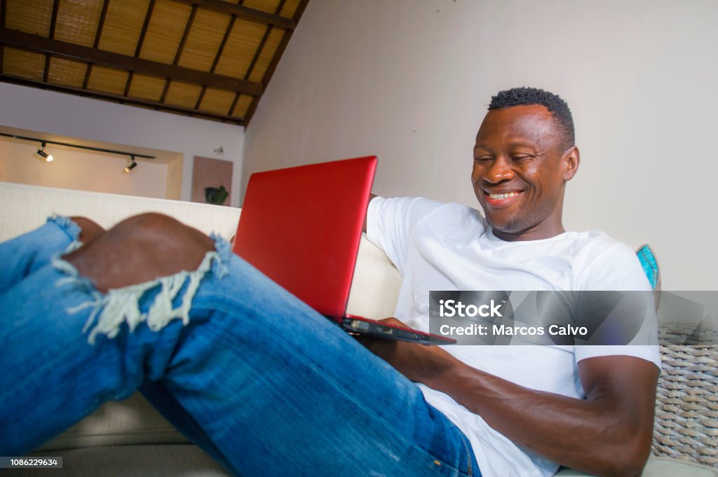 young attractive and happy successful black African American man networking with laptop computer at living room couch smiling cheerful and satisfied in internet business success concept 30-39 Years Stock Photo