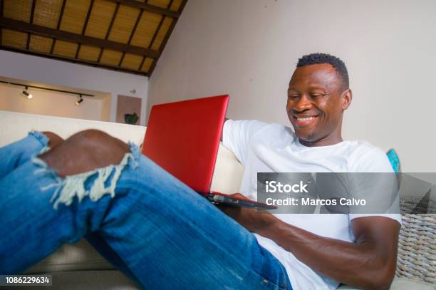 Young Attractive And Happy Successful Black African American Man Networking With Laptop Computer At Living Room Couch Smiling Cheerful And Satisfied In Internet Business Success Concept Stock Photo - Download Image Now