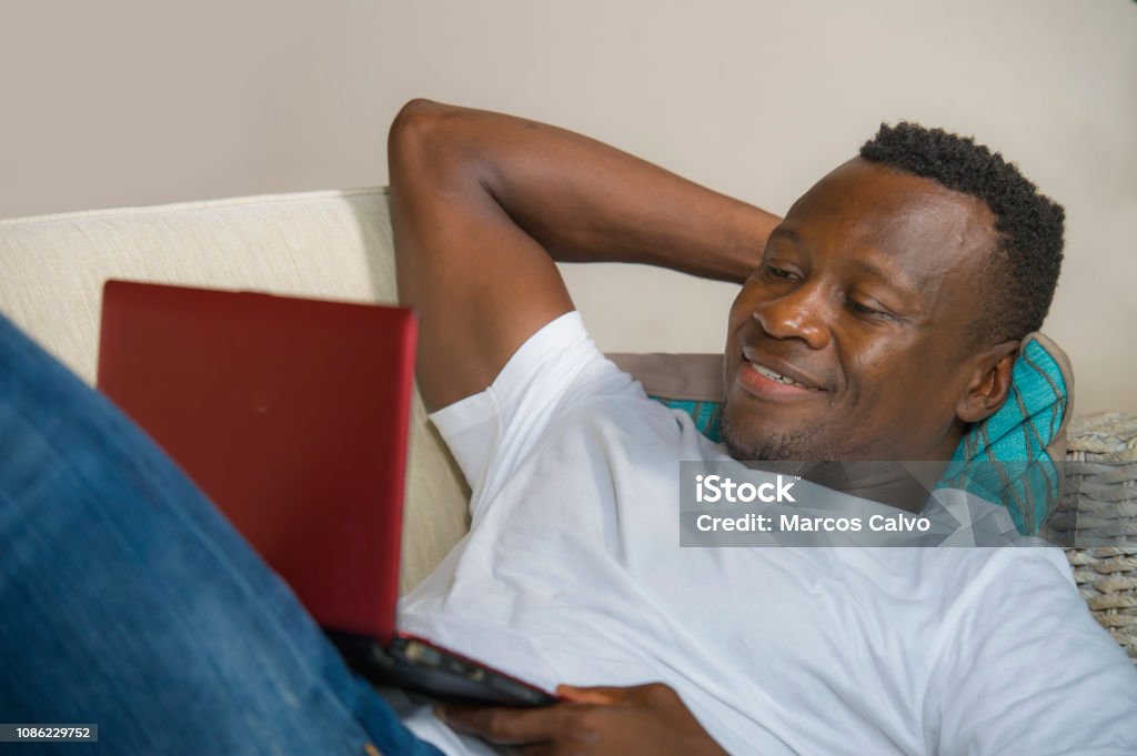 young attractive and happy successful black African American man networking with laptop computer at living room couch smiling cheerful and satisfied in internet business success concept 30-39 Years Stock Photo