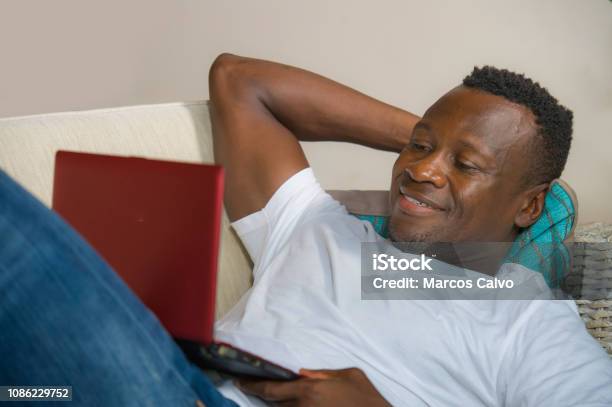 Young Attractive And Happy Successful Black African American Man Networking With Laptop Computer At Living Room Couch Smiling Cheerful And Satisfied In Internet Business Success Concept Stock Photo - Download Image Now