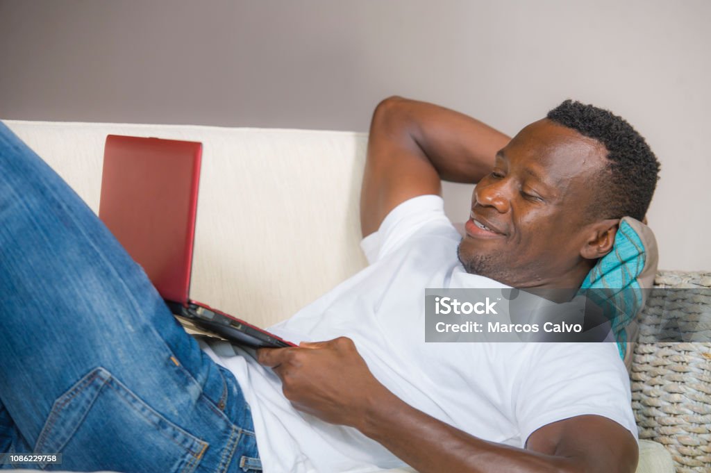 young attractive and happy successful black afro American man networking with laptop computer at living room couch smiling cheerful and satisfied in internet business success concept 30-39 Years Stock Photo