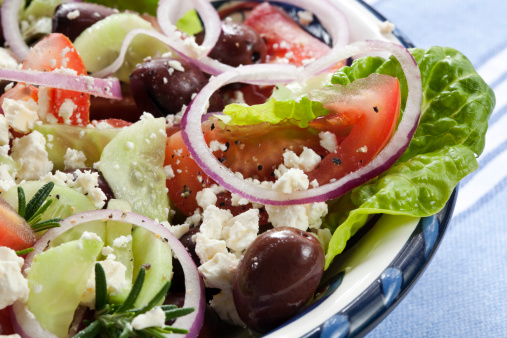 Close-up of bowl of Greek salad.  Luscious vine-ripened tomatoes, with feta cheese, kalamata olives, cucumber, red onion, kos lettuce and rosemary.  More salads:
