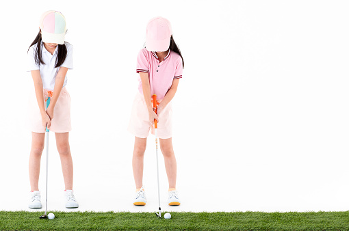 Brother and sister Asian in sportswear and colorful hats are happy with pose the way they play golf on astroturf isolated on white background.