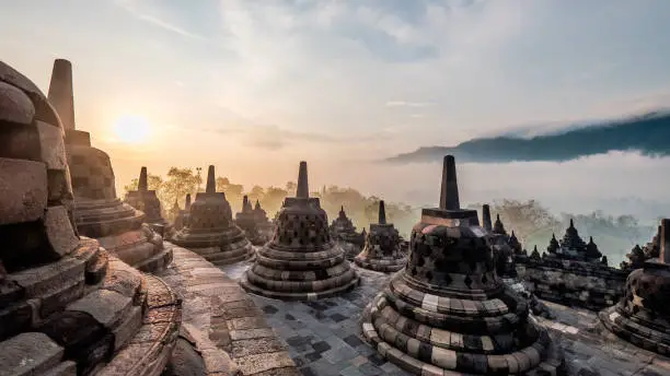 Shot of sunrise on a misty day at Borobudur Temple with stupas lined in a circular row - Indonesia.