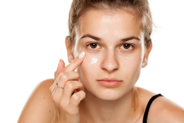 istock Young woman applying cream on her face on white background 1086242904