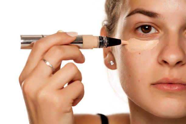 istock Young woman applying concealer under her eyes on white background 1086265624