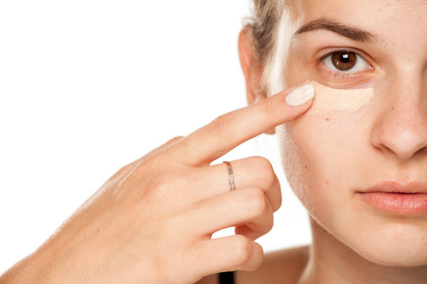 Young woman applying concealer under her eyes on white background Young woman applying concealer under her eyes on white background concealer stock pictures, royalty-free photos & images