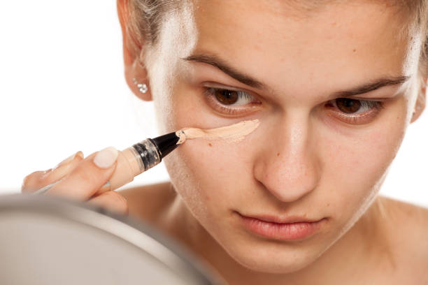 istock Young woman applying concealer under her eyes on white background 1086265640