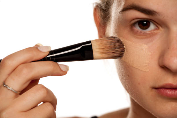 istock Young woman applying liquid foundation with brush on white background 1086265648
