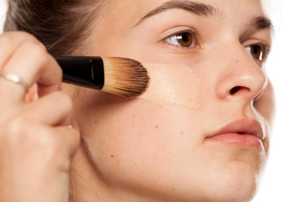 istock Young woman applying liquid foundation with brush on white background 1086265658