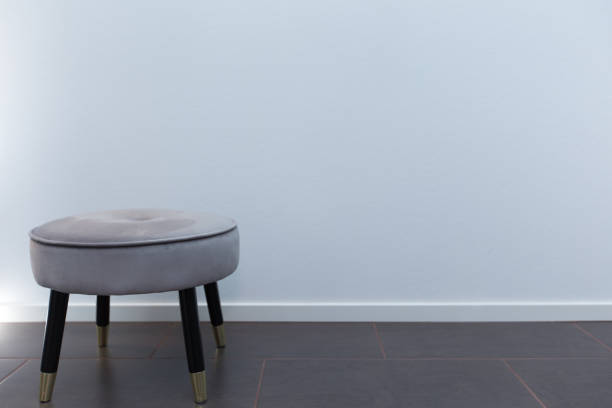 Luxury small chair in front of white wallpaper, standing to the side on limestone floor with light stock photo