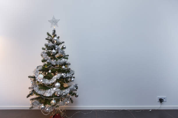 Small Christmas tree standing in front of white wallpaper plugged in and shining stock photo