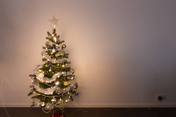 Small Christmas tree standing in front of white wallpaper plugged in and shining warm stock photo