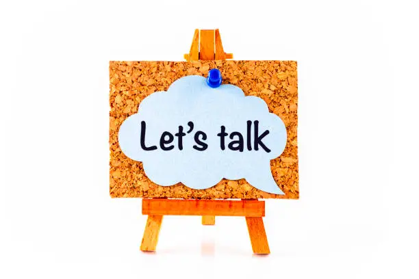 Blue speech bubble with phrase Let`s Talk on corkboard on wooden easel. White background