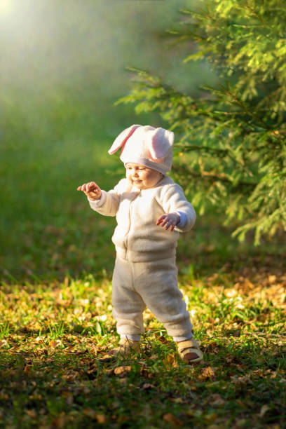 bambina in tuta da coniglietto in piedi contro la luce del sole nella foresta - baby first steps autumn child foto e immagini stock