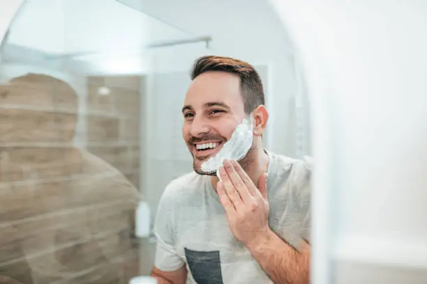 Handsome man applying shaving cream, reflection in the mirror image.