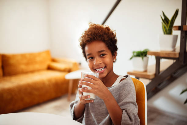 portrait of a smiling little african american girl with a glass of milk at home. - milk child drinking little girls imagens e fotografias de stock