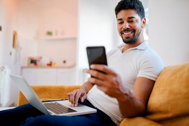 istock Handsome african american man using laptop and mobile phone at home. 1086350932
