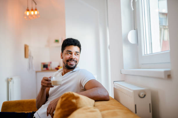 istock Handsome african american man drinking coffee and looking through window at home. 1086351020