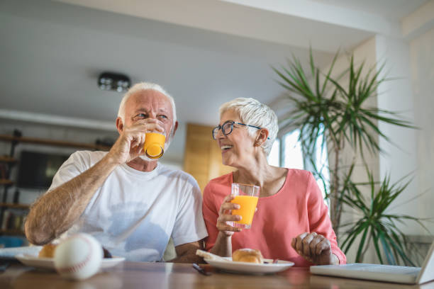 coppia anziana che beve succo d'arancia durante la colazione - 60s senior adult breakfast cheerful foto e immagini stock