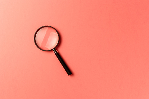 Magnifying glass on coral background. Top view. Flat lay. Copy space. New minimal creative concept. Living Coral color of the Year 2019