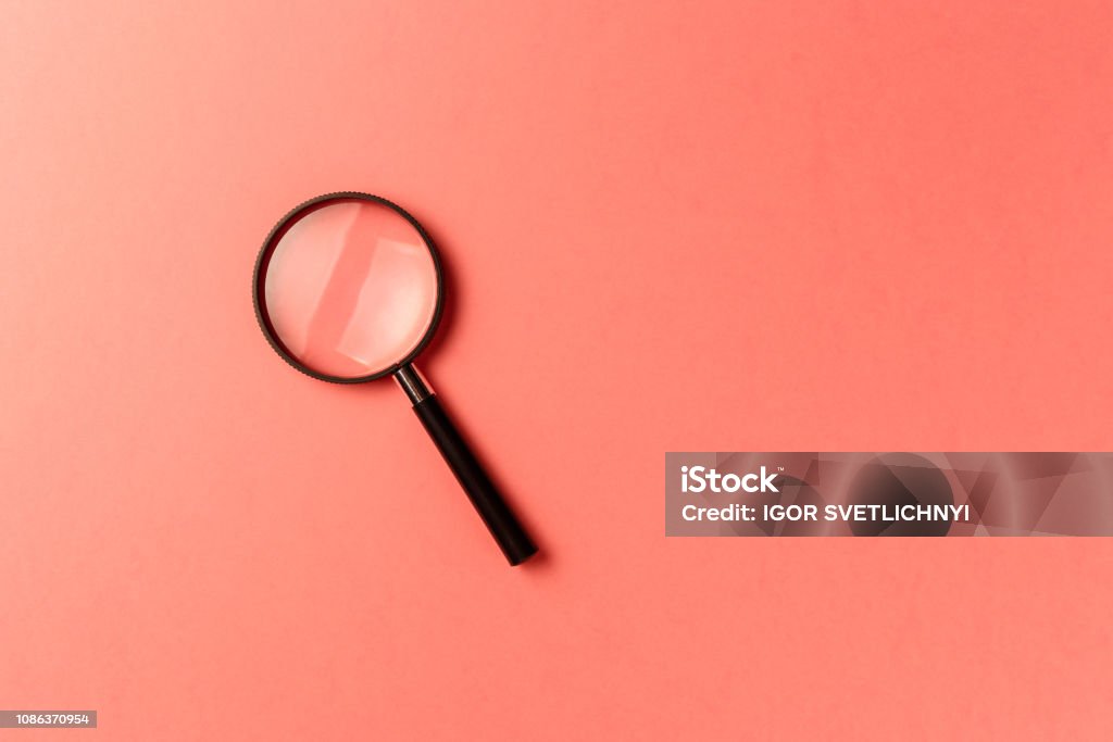 Magnifying glass on coral background. Top view. Flat lay. Copy space. New minimal creative concept. Living Coral color of the Year 2019 Magnifying Glass Stock Photo