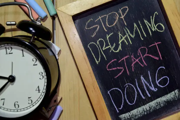 Photo of STOP DREAMING START DOING on phrase colorful handwritten on chalkboard