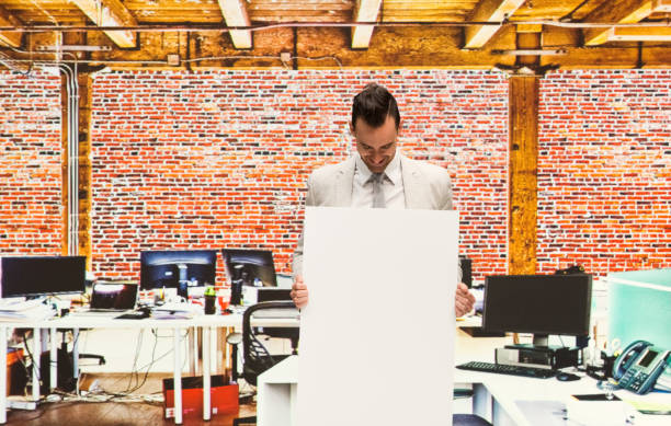 istock Attractive businessman standing at work holding a white cardboard sign 1086397200