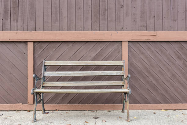 Empty wooden bench against paneled wall on sidewalk of an overcast day