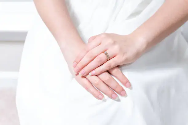 Closeup of hands of young female person, woman, bride in wedding dress, sitting by window, white curtains with engagement diamond ring on finger of hands