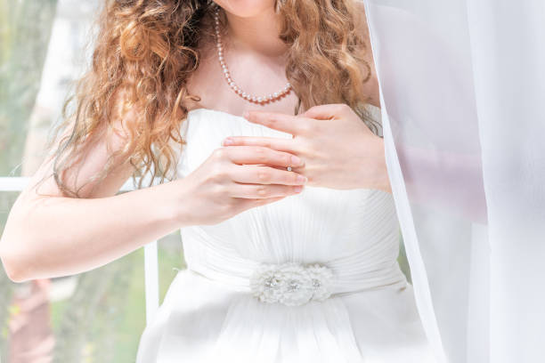 closeup portrait der jungen weiblichen person, frau, braut hochzeit kleid, perlenkette, stehen durch fenster, weiße vorhänge, diamant-verlobungsring von finger mit händen ausziehen - pearl jewelry necklace women stock-fotos und bilder