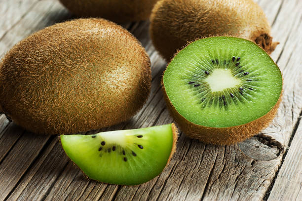 kiwi fresco maturo a fette, metà intero e pezzo frutta kiwi succosa biologica su sfondo di legno - kiwi foto e immagini stock