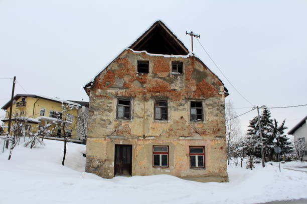 istock Abandoned ruined house with broken windows and fallen facade covered in snow 1086446020
