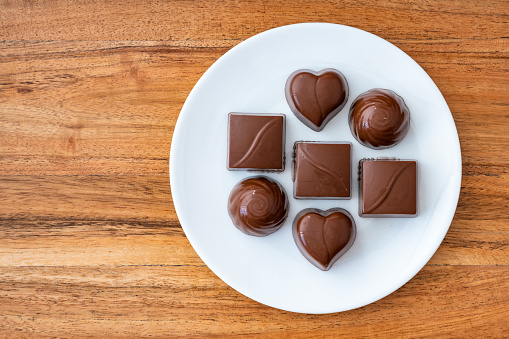 Assorted milk chocolate candy on a white plate on a wood background for Valentine’s Day