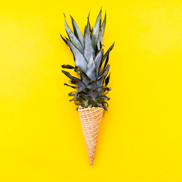 istock Ice cream cone with pineapple leaves on bright yellow background flat lay top view 1086521592