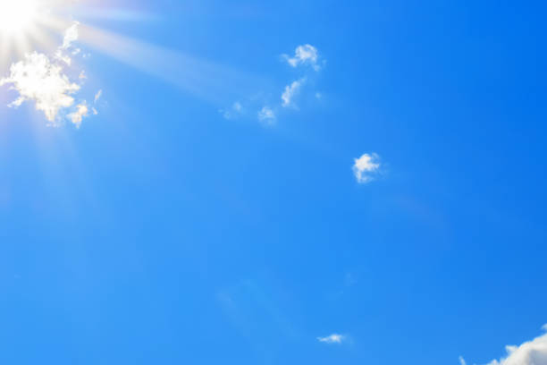 Bright sun with beautiful beams in the blue sky with some light clouds. Space for copy.