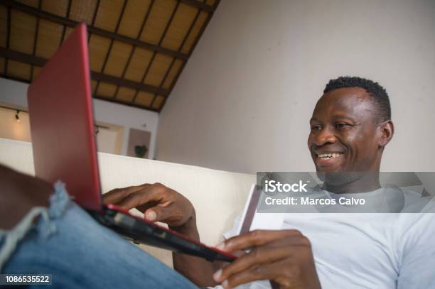 Lifestyle Portrait Of Young Happy And Attractive Black Afro American Man Using Credit Card And Laptop Computer Relaxed And Cheerful At Living Room Sofa Couch Internet Banking And Online Shopping Stock Photo - Download Image Now