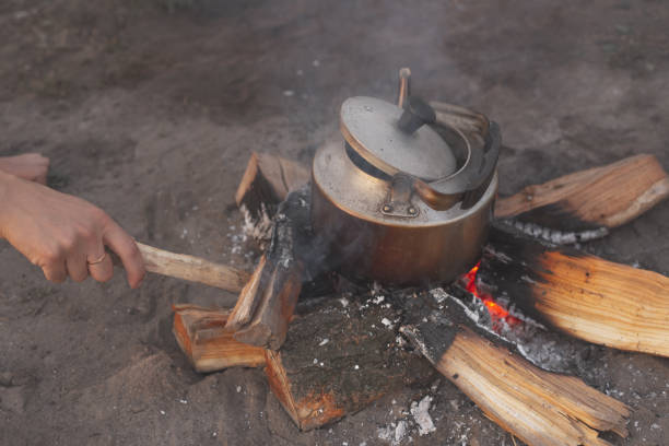 istock the hand of a guy fixes a fire with a stick on which the kettle is boiling 1086550852