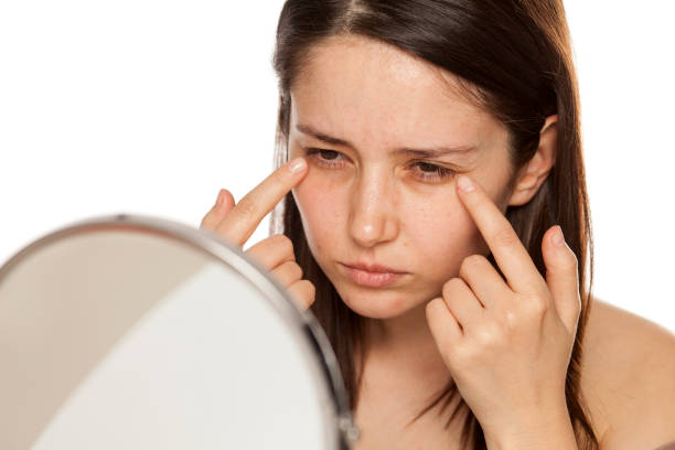 istock Beautiful young woman touch her face under eyes in mirror on white background 1086566832