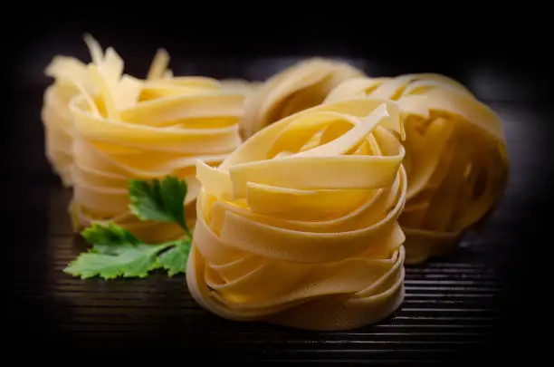 Traditional dry fettuccine pasta on dark wooden background. Selective focus.