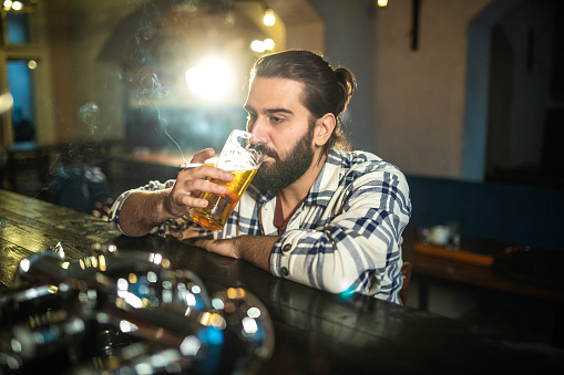 Handsome Bearded drunk Man drinking beer and smoking cigarette
