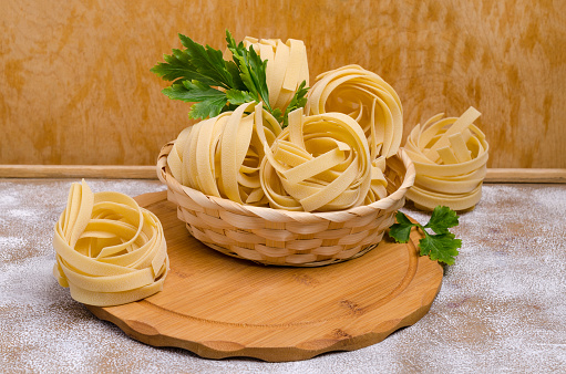 Traditional dry fettuccine pasta on brown wooden background. Selective focus.