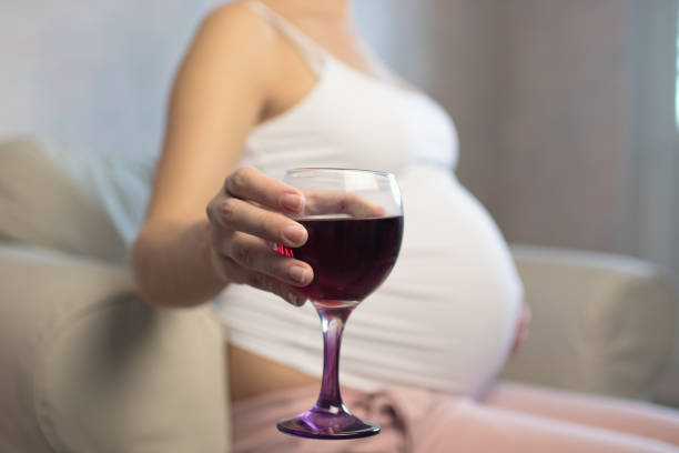 donna incinta con bicchiere di vino rosso in mano all'interno - abdomen addiction adult alcohol foto e immagini stock